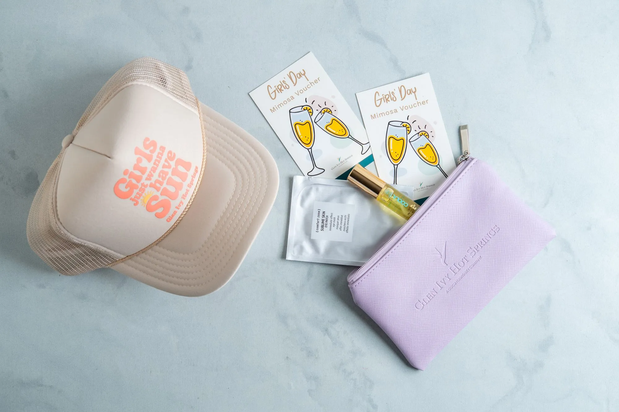 A beauty kit with &ldquo;Girls Day&rdquo; mimosa voucher cards, a small bottle, and two toiletry pouches on a light blue surface.