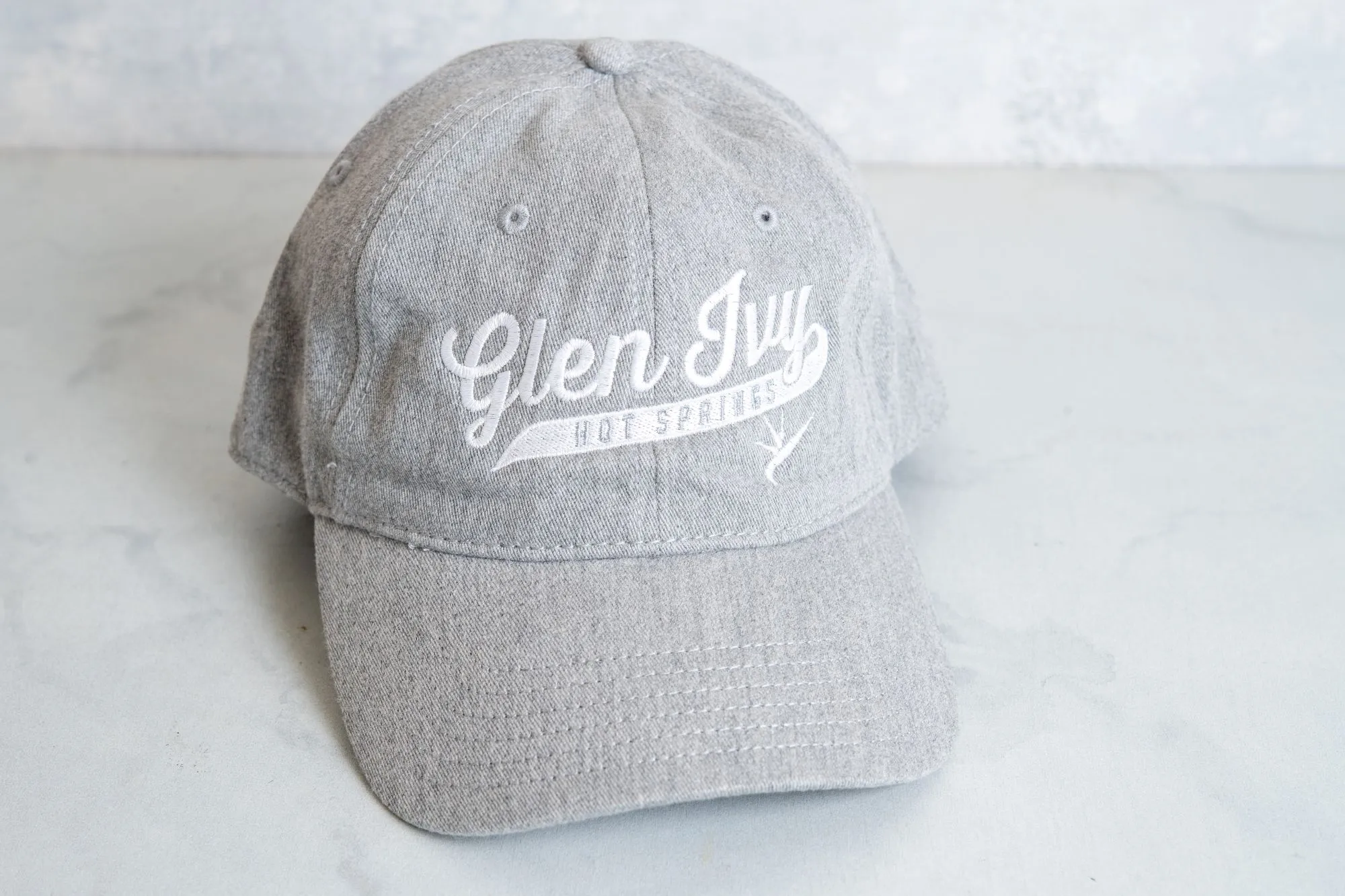 A gray baseball cap with the word &ldquo;glen sly&rdquo; and small animal icons, photographed on a light background.