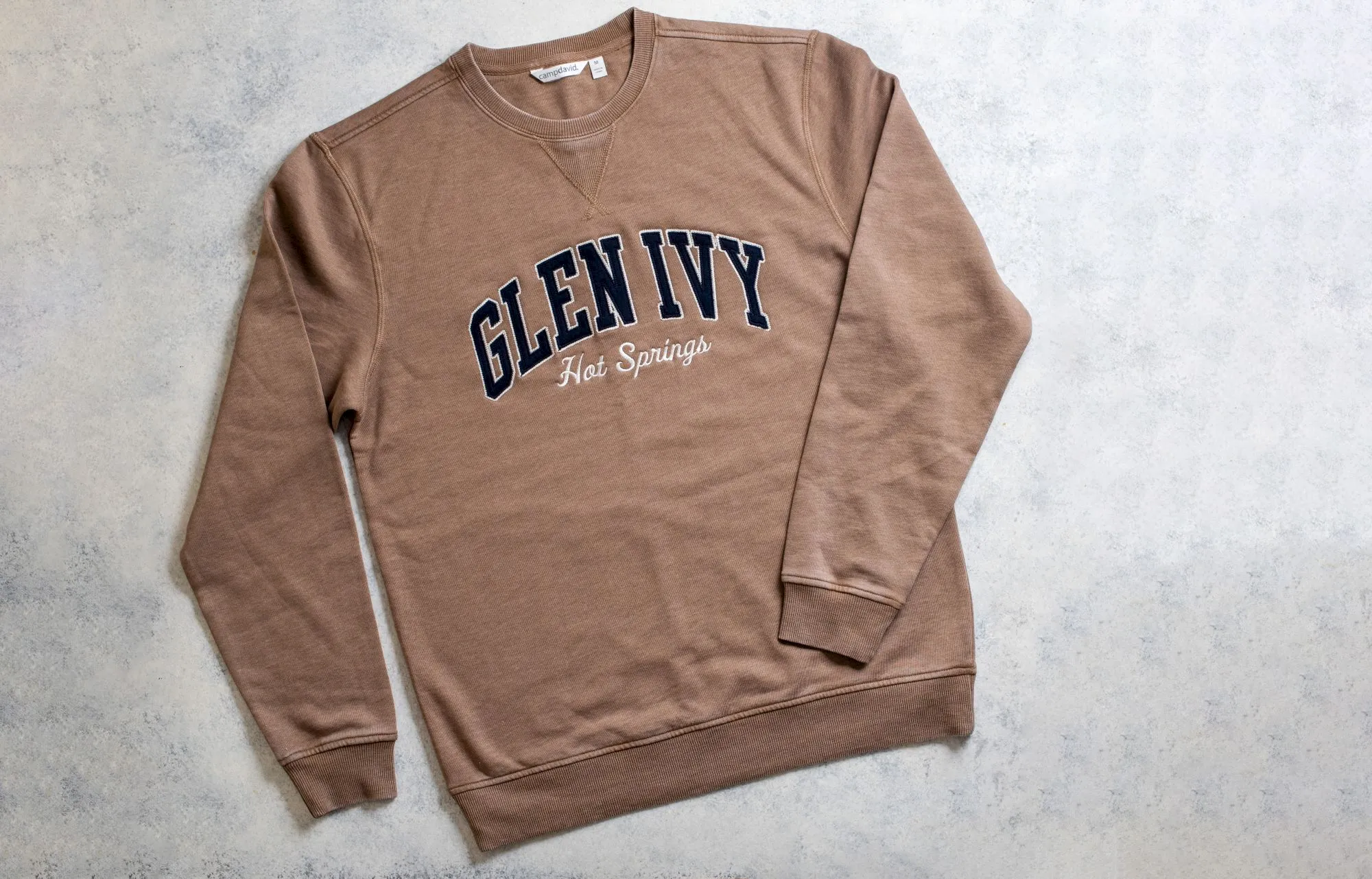 A brown sweatshirt lies flat, with &ldquo;GLENNY&rdquo; and &ldquo;Hot Springs&rdquo; printed across the chest in bold lettering.