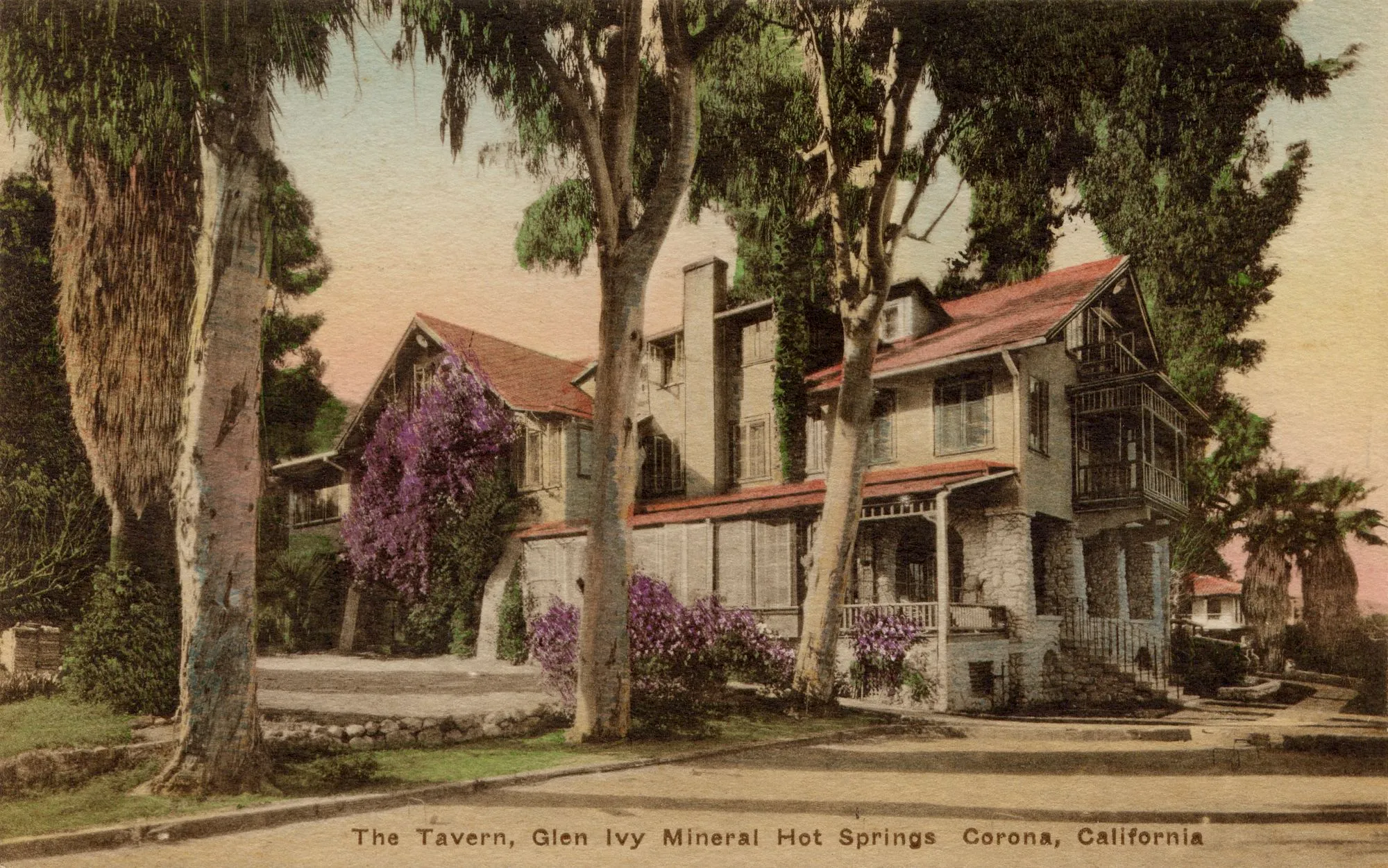 A vintage postcard shows a resort-like building surrounded by tall trees and purple flowering shrubs at The Tavern, Glen Ivy Mineral Hot Springs, Corona, California.