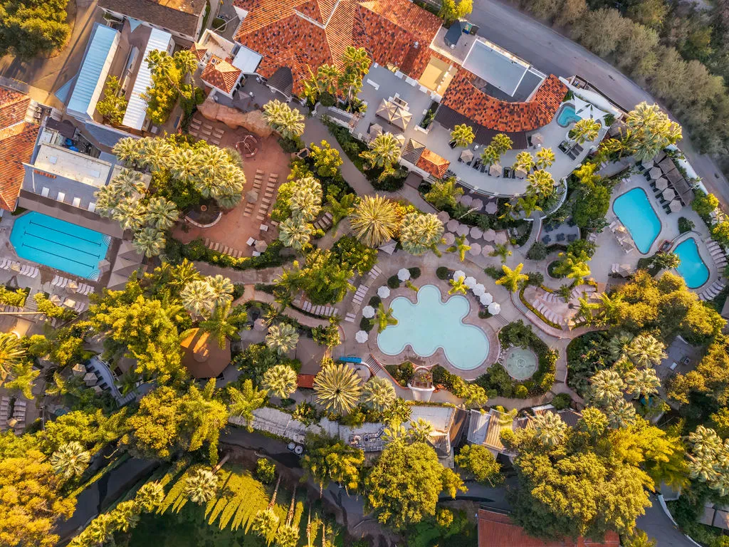Aerial view of a tropical resort with brick rooftops, lush palm gardens, and multiple swimming pools.